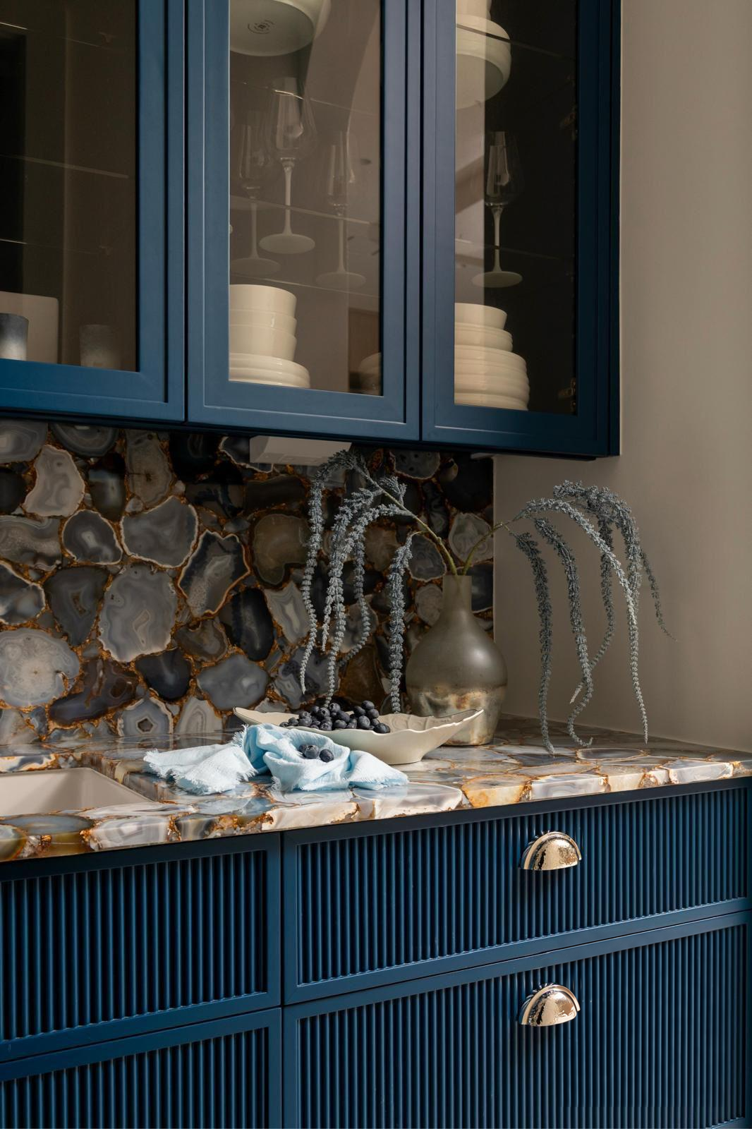 Blue fluted cabinetry with a patterned natural stone backsplash and counter
